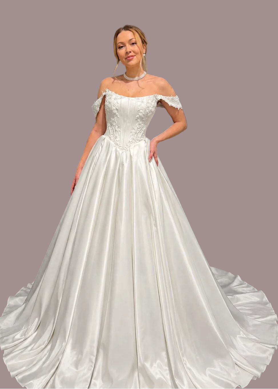 An off-the-shoulder white satin ball gown with a structured lace bodice with beaded detail and a full train against 