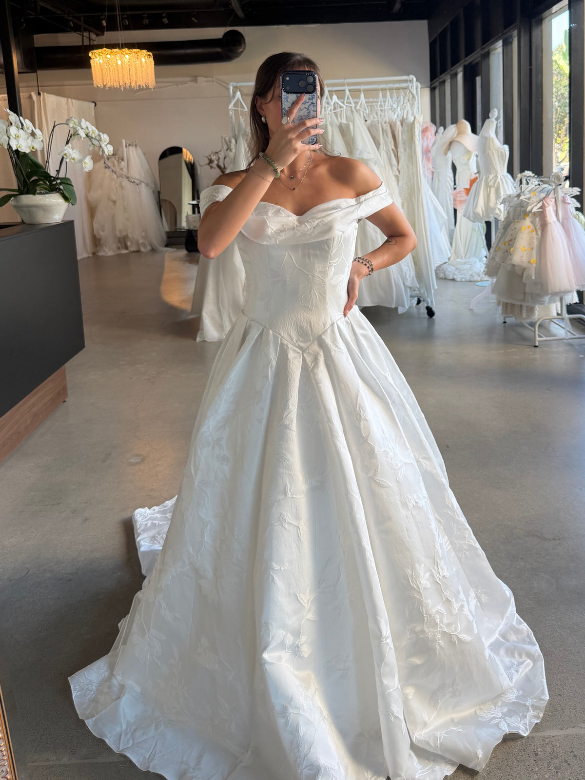 a voluminous off-the-shoulder white wedding gown with a fitted bodice and full ball gown skirt. 
