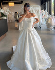 a voluminous off-the-shoulder white wedding gown with a fitted bodice and full ball gown skirt. 