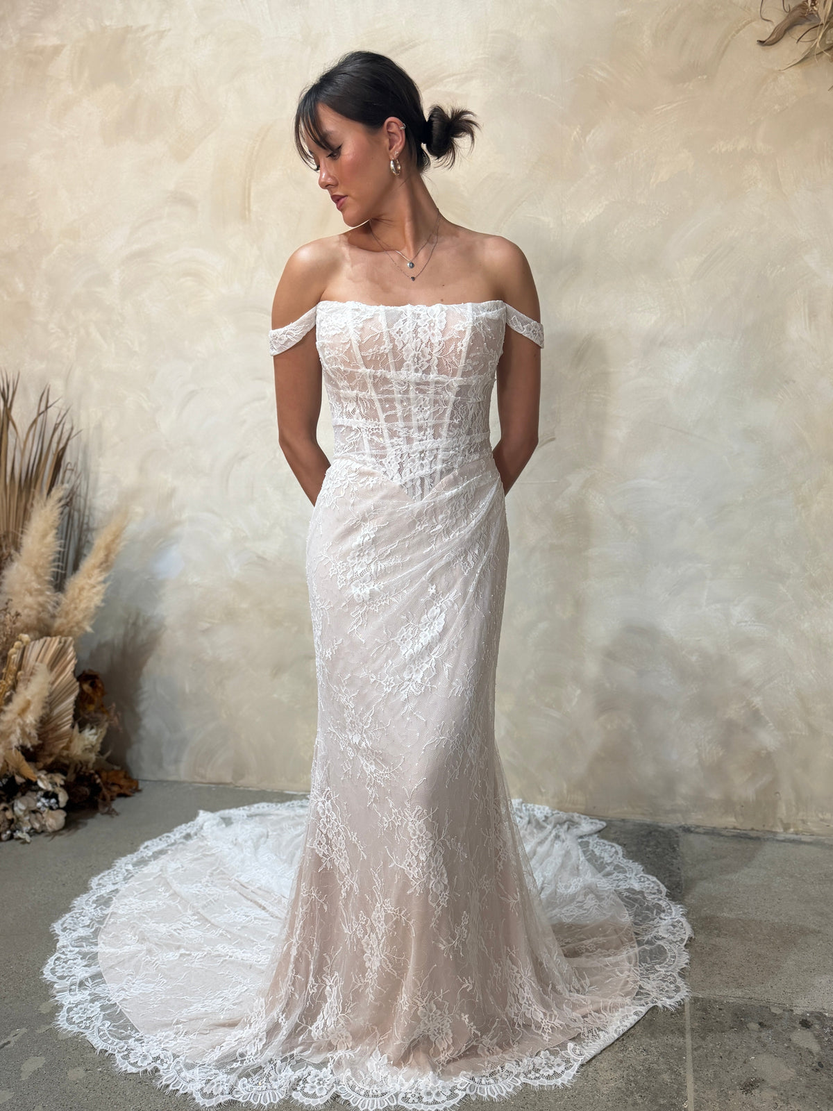 An off-the-shoulder lace wedding gown with a structured corset bodice and a long train