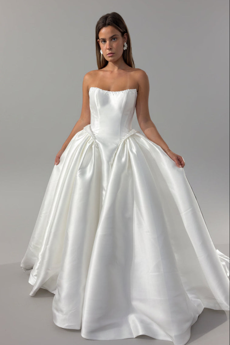 A woman modeling a strapless white ball gown wedding dress with a structured bodice and voluminous satin ballgown dress