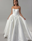 A woman modeling a strapless white ball gown wedding dress with a structured bodice and voluminous satin ballgown dress